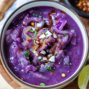 Vibrant purple red cabbage soup in a white bowl, garnished with cream and red pepper flakes.