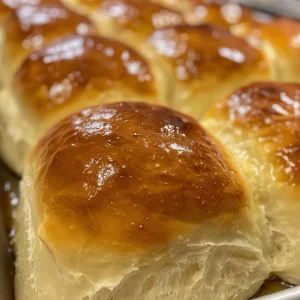 A plate of freshly baked dinner rolls, glistening with a light sheen.