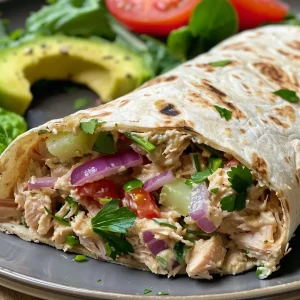 ['Close-up view of a high-protein tuna salad wrap filled with fresh ingredients.', 'Side view of a delicious tuna salad wrap showcasing vibrant vegetables and creamy filling.', 'Juicy tuna salad wrap with layers of greens, tomato, and avocado, presented in a tortilla.', 'High-protein tuna salad wrap prepared with whole wheat tortillas and colorful ingredients.']