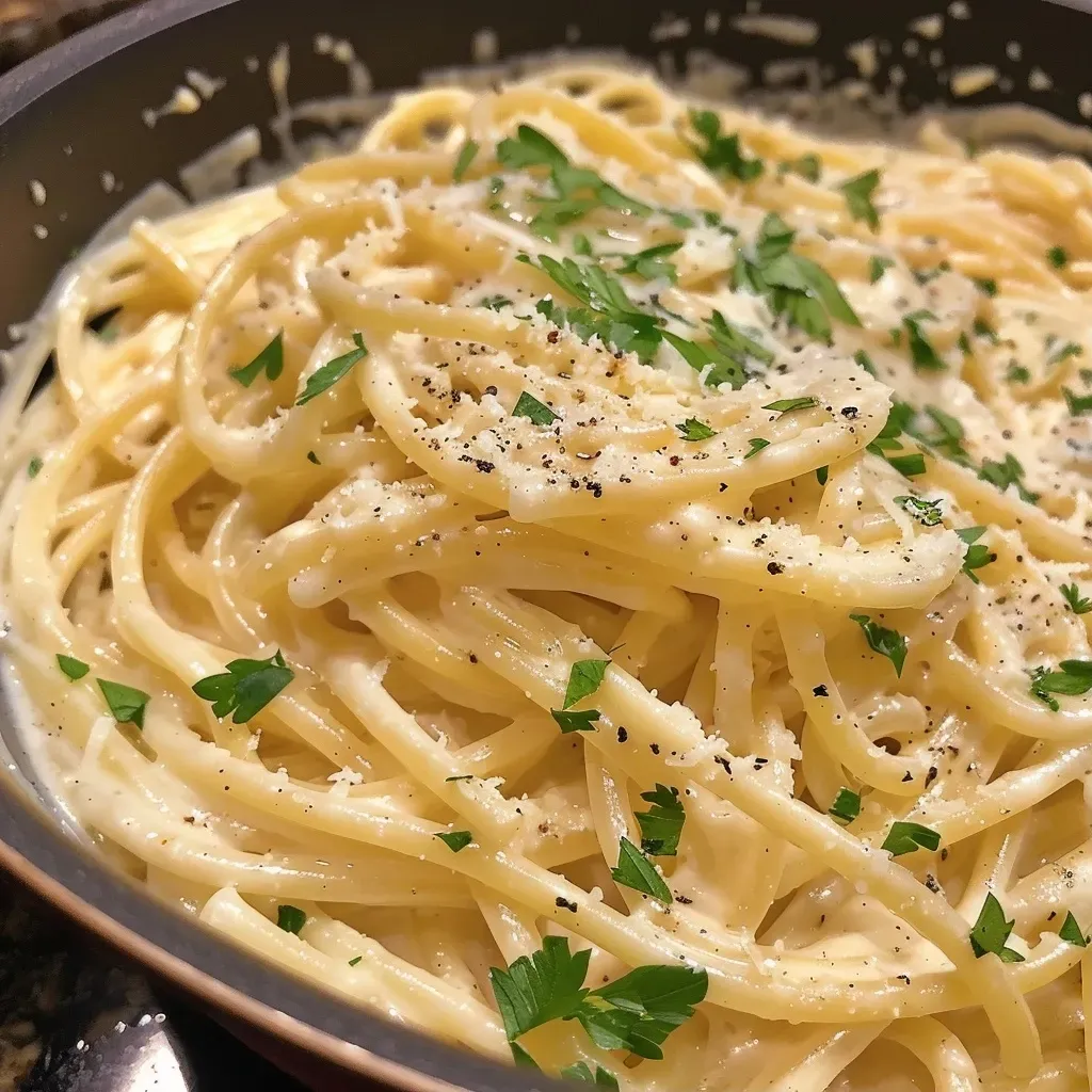 ['Close-up view of creamy garlic pasta topped with freshly grated Parmesan and herbs.', 'Juicy One Pot Creamy Garlic Pasta dish with a rich sauce and garlic cloves visible.', 'Side view of a bowl filled with creamy garlic pasta, glistening in natural light.', 'Delicious creamy pasta with garlic, salt, and pepper, garnished with green herbs.']