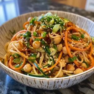 ['Close-up view of cold sesame noodles topped with spiralized zucchini and carrots, garnished with green onions and sesame seeds.', 'Juicy cold sesame noodles served with colorful spiralized vegetables, featuring a vibrant mix of greens and oranges.', 'A detailed side view of cold sesame noodles with chickpeas and fresh vegetables, showcasing their rich textures.', 'Freshly prepared cold sesame noodles garnished with sesame seeds and sliced green onions, surrounded by spiralized veggies.']