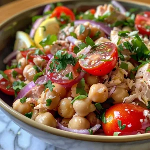['A close-up view of a colorful Lemony Chickpea and Tuna Salad in a bowl.', 'Side view of a vibrant salad featuring chickpeas, tuna, and fresh herbs.', 'Close-up image of a refreshing salad with chickpeas, tomatoes, and lemon dressing.', 'Detail shot of a nutritious Lemony Chickpea and Tuna Salad garnished with herbs.']
