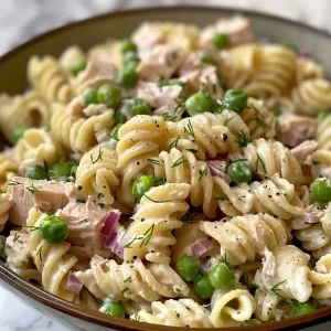 ['Close-up view of a colorful tuna pasta salad with shells, peas, and vegetables.', 'Side view of a delicious bowl of Old Fashioned Tuna Pasta Salad showcasing its creamy texture.', 'Vibrant tuna pasta salad featuring medium pasta shells, peas, and diced vegetables.', 'Close-up shot of a hearty tuna pasta salad with mayo, Greek yogurt, and fresh herbs.']