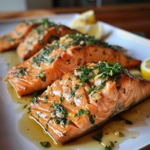 Close-up side view of a juicy Garlic Herb Roasted Salmon garnished with herbs and lemon.