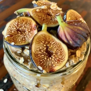 ['Close-up of a Mason jar filled with Maple Fig Tahini Overnight Oats.', 'Side view of overnight oats layered with figs and tahini in a glass jar.', 'Delicious Maple Fig Tahini Overnight Oats in a jar, showing oats and fruit.', 'Wooden table setting with a Mason jar of creamy Maple Fig Tahini Overnight Oats.']