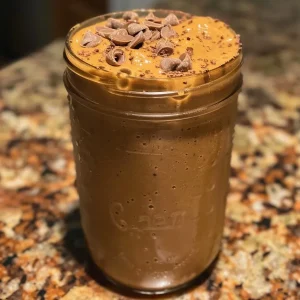 ['Close-up view of a pumpkin peanut butter cup smoothie in a glass.', 'Side view of a creamy pumpkin smoothie topped with swirls of peanut butter.', 'Thick and rich pumpkin peanut butter cup smoothie presented in a clear glass.', 'Smoothie featuring vibrant orange pumpkin color and dark chocolate accents.']
