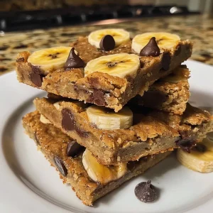 ['Close-up side view of moist banana blondies with chocolate chips.', 'Tasty 4-ingredient banana blondies displayed on a plate, showing a soft texture.', 'Golden-brown banana blondies highlighted, showcasing their chewy consistency.', 'Freshly baked banana blondies topped with chocolate chips, presented in a natural light.']