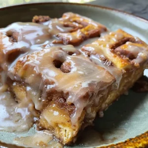 ['Close-up of a slice of cinnamon roll casserole topped with icing.', 'Side view of Crockpot Cinnamon Roll Casserole showing its fluffy texture.', 'Juicy, golden-brown cinnamon roll casserole in a crockpot.', 'A decadent serving of cinnamon roll casserole with icing drizzled on top.']