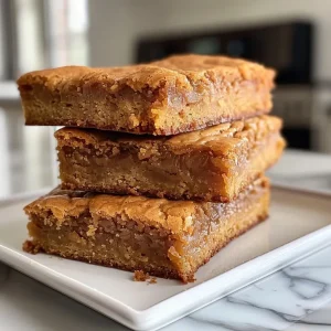 ['Close-up image of a golden-brown blondie, showing a dense texture with chocolate chips.', 'Side view of a freshly baked blondie, highlighting its moist surface and rich color.', 'Juicy easy blondie showcased with a shiny glaze, taken with a smartphone.', 'Detailed close-up of a blondie cut into squares, revealing a fudgy interior.']