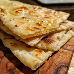 ['Close-up image of golden brown flatbread on a wooden surface.', 'Side view of a soft, fluffy flatbread with a slight shine.', 'Tasty flatbread displayed with a rustic background.', 'Homemade flatbread with a crispy edge and soft center.']