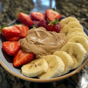 ['A close-up shot of a creamy peanut butter fruit dip in a bowl, served with fresh fruits.', 'Side view of a delectable peanut butter dip, surrounded by sliced fruits for dipping.', 'Close-up of a rich peanut butter fruit dip, highlighting its smooth texture alongside vibrant fruits.', 'A mouth-watering peanut butter dip displayed in a bowl, with a variety of fresh fruit pieces beside it.']