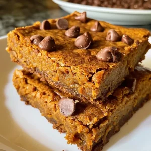 ['Close-up of golden Pumpkin Blondies with chocolate chips on a plate.', 'Side view of moist Pumpkin Blondies showcasing their rich texture and chocolate chips.', 'Detailed shot of Pumpkin Blondies, highlighting the buttery surface and chocolate morsels.', 'Close-up perspective of delicious Pumpkin Blondies featuring a warm, inviting color.']