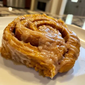 ['Close-up of gluten and sugar-free pumpkin protein cinnamon rolls on a plate.', 'Side view of moist pumpkin protein cinnamon rolls with a creamy glaze.', 'Delicious pumpkin cinnamon rolls displayed on a rustic wooden table.', 'A stack of pumpkin protein cinnamon rolls with pumpkin puree and spices.']